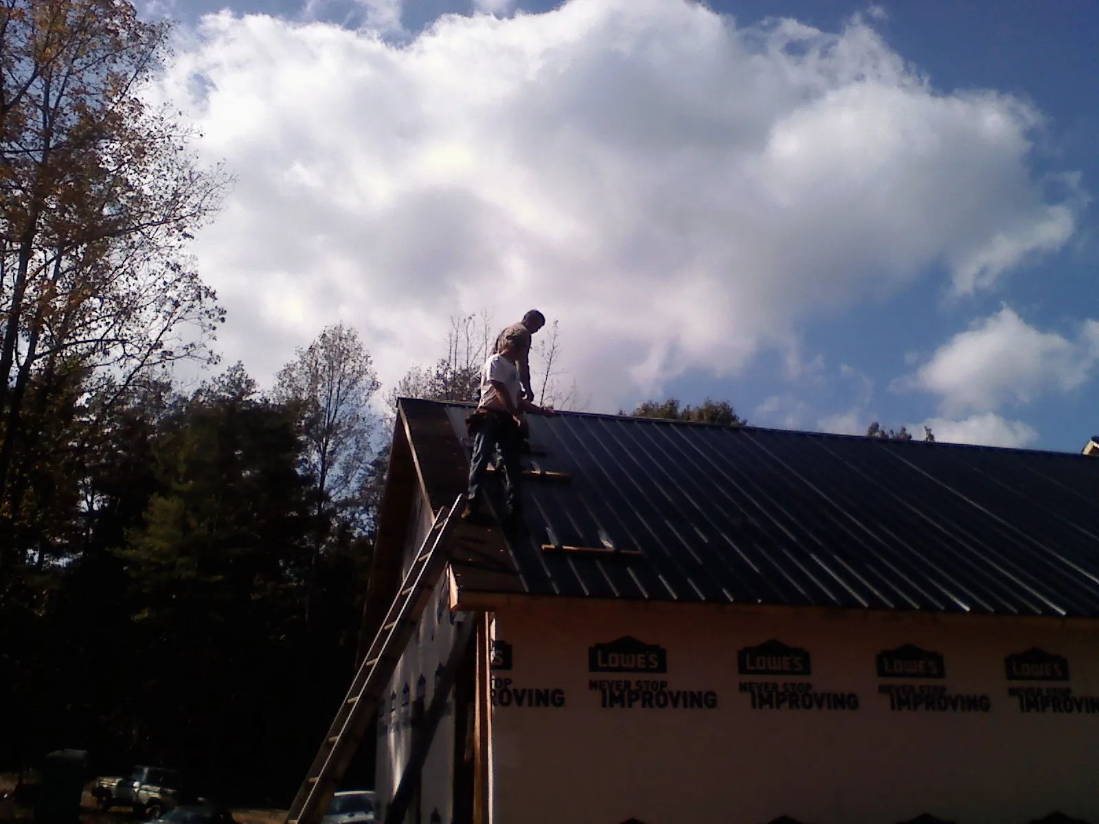 Roofer fastening dark metal panels high against a cloudy sky, from a Roof Inspection job in Scranton