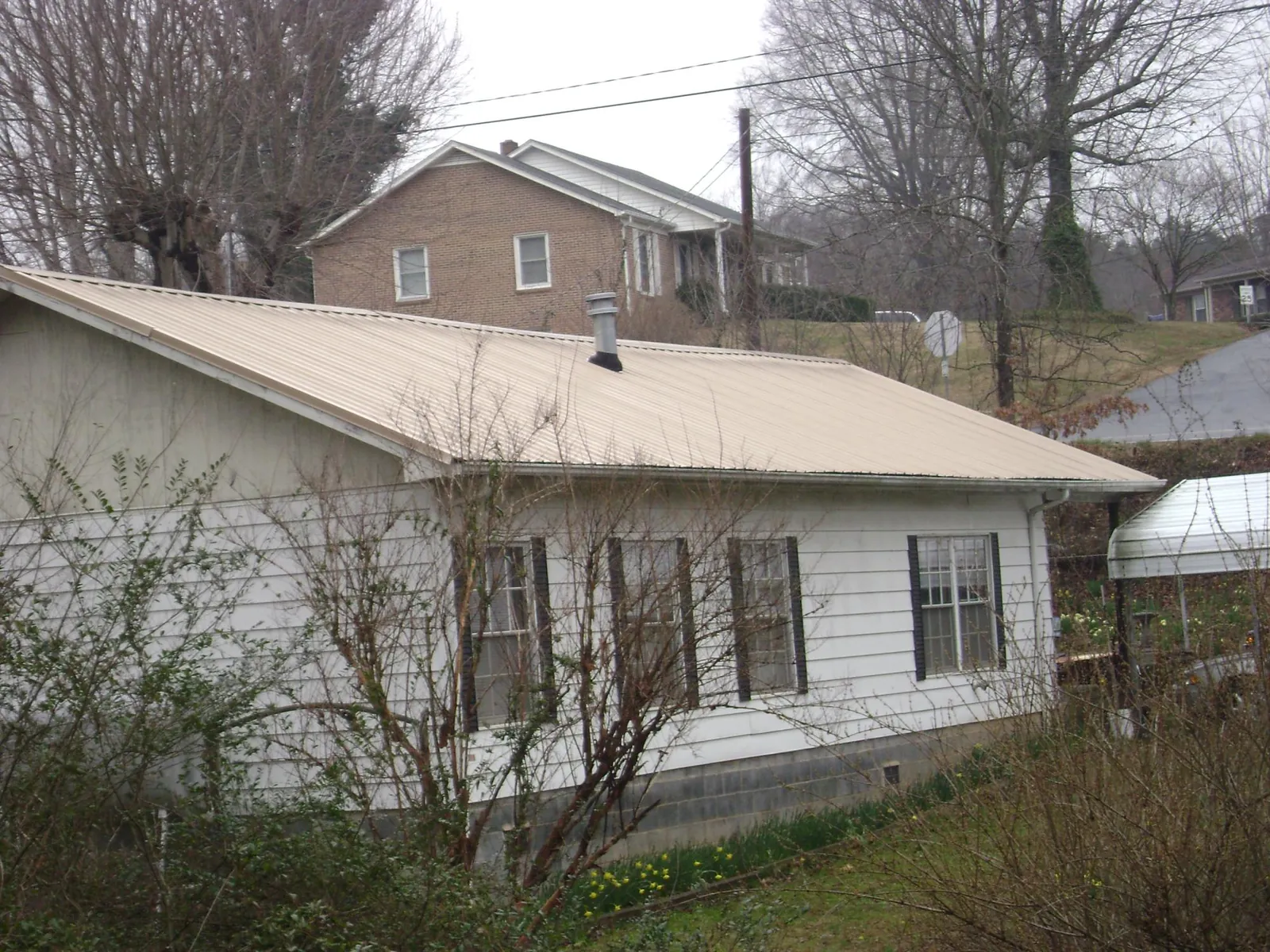 Tan metal roof on a white sided house set into a hillside — Commercial Roofing by Roofing Brothers in Scranton